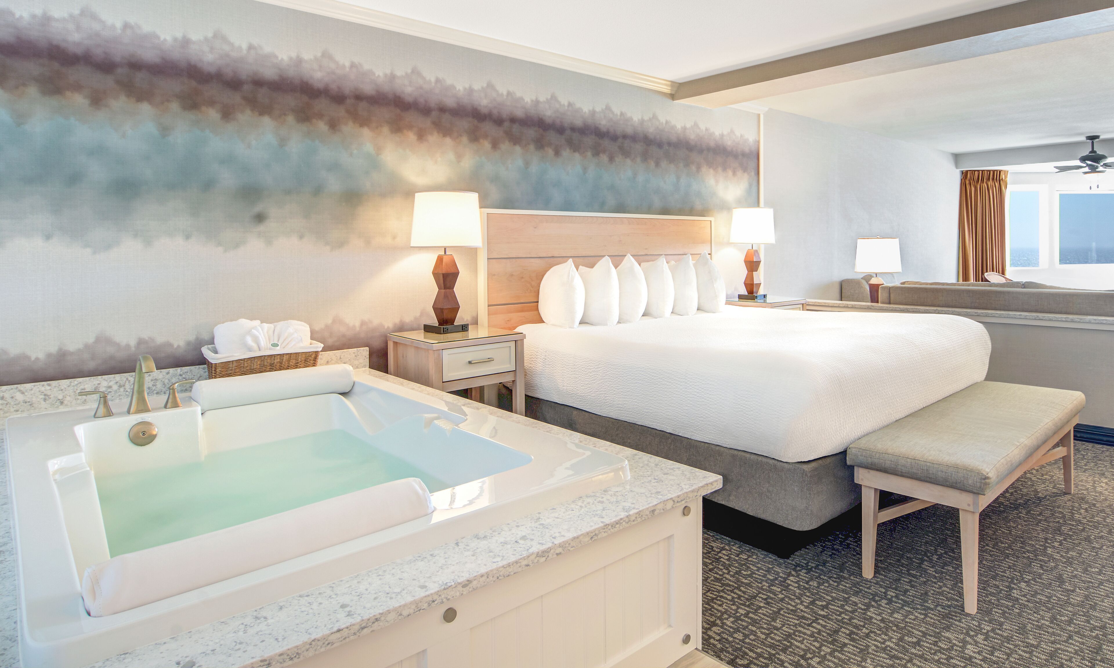 Een hotelkamer met een groot bed, een zithoek, een badkuip en uitzicht op de stad.