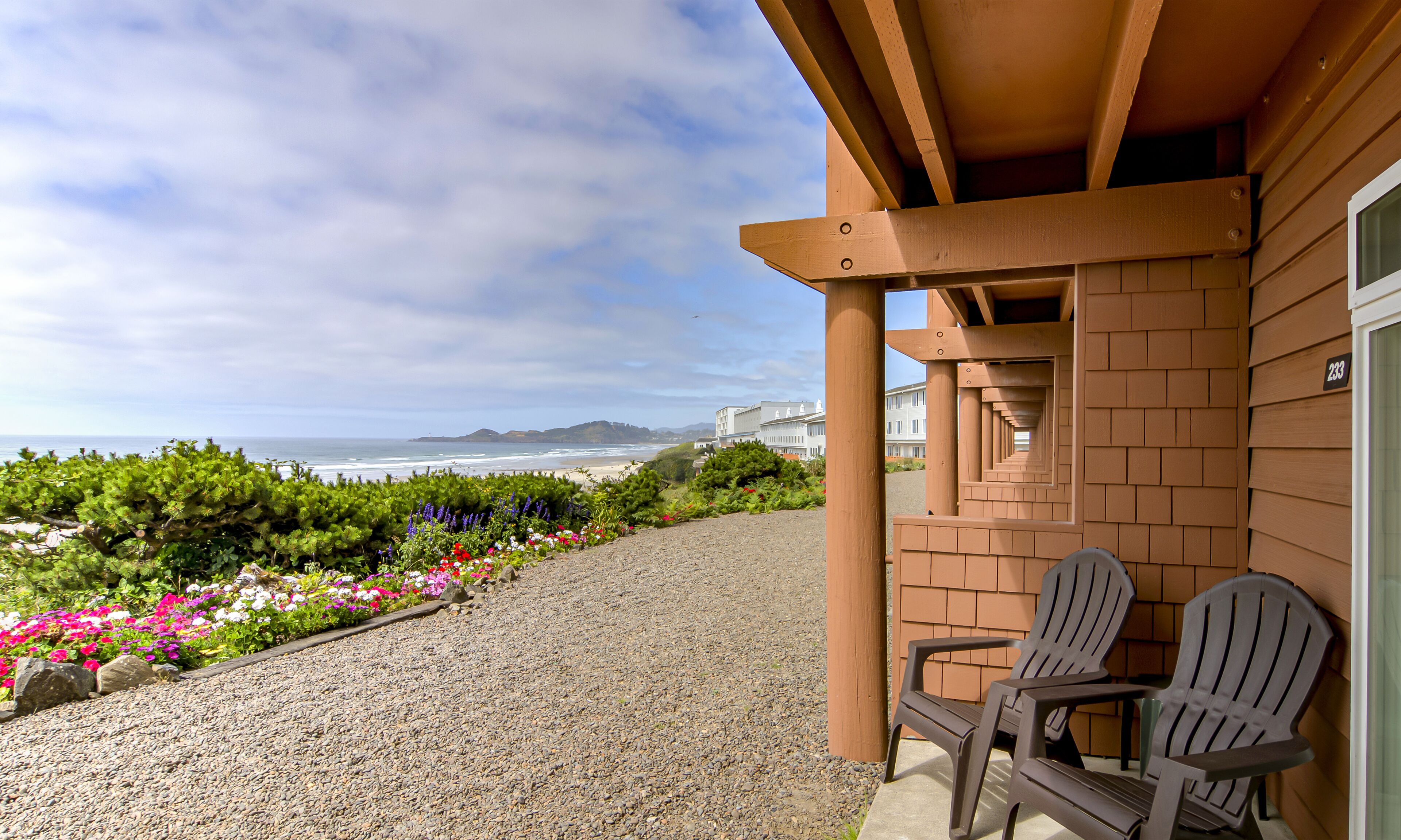 A balcony with two Adirondack chairs overlooking a beach with a view of the ocean and distant hills.