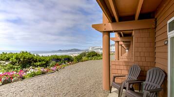 A balcony with two Adirondack chairs overlooking a beach with a view of the ocean and distant hills.