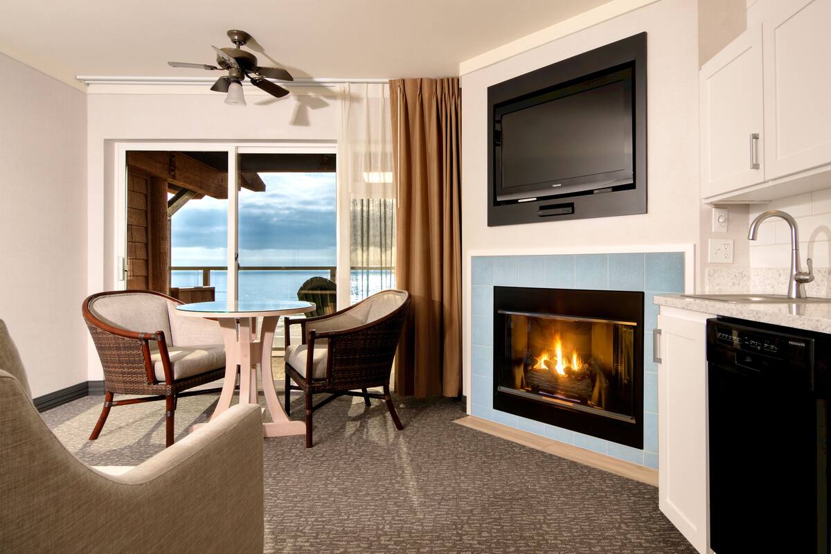 A modern kitchen with a fireplace, a dining area with a view of the ocean, and a ceiling fan.