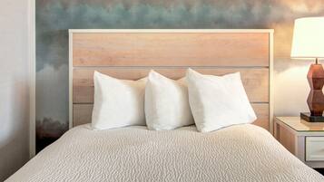 Una cama con cubierta blanca texturizada, cabecera de madera y tres almohadas blancas.