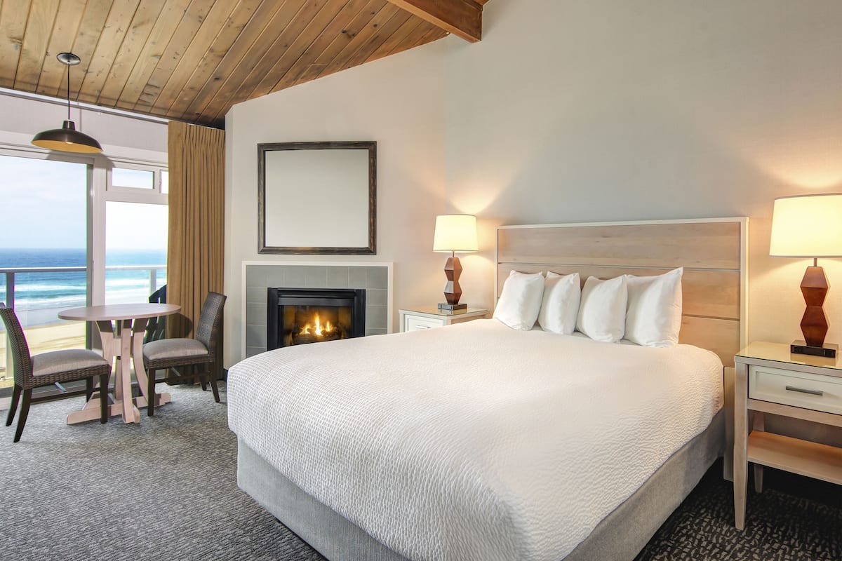 A hotel room with a large bed, a fireplace, a dining table with chairs, and a view of the ocean.