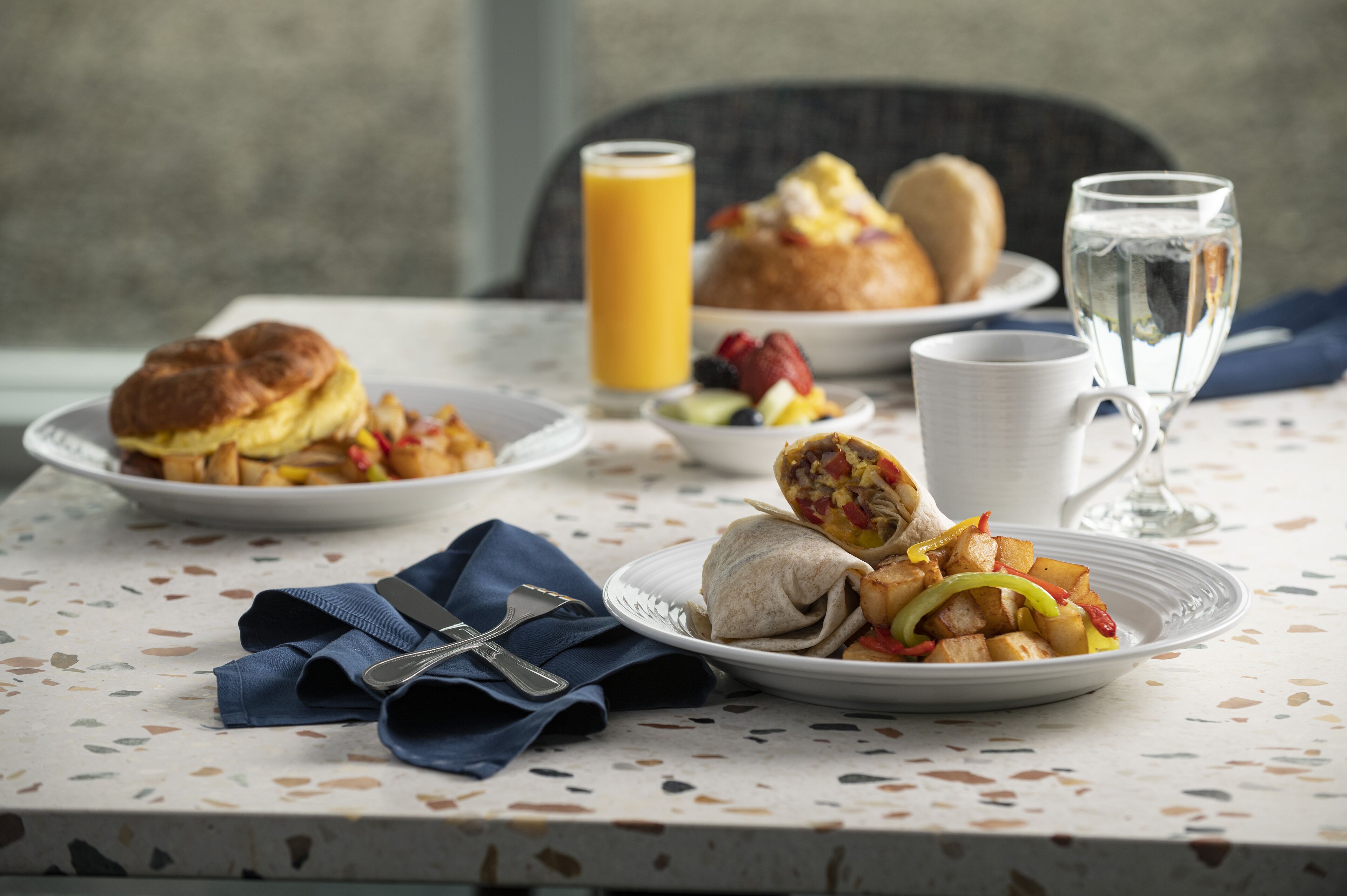 A breakfast table with plates of food, a glass of orange juice, a glass of water, and a cup.