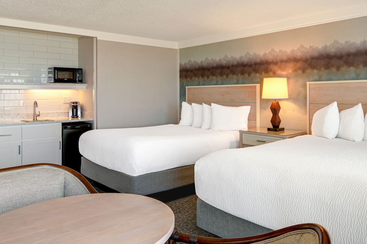 A hotel room with two beds, a dining table, a microwave, and a coffee maker.