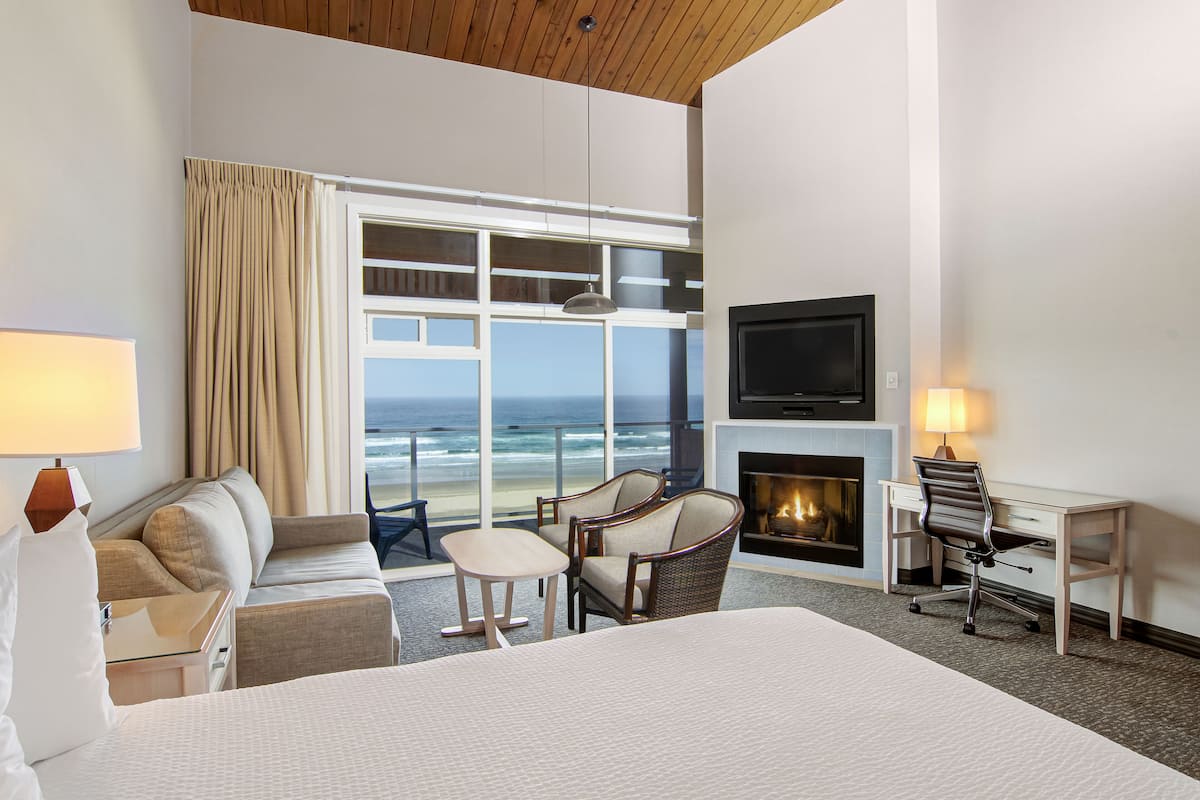 A hotel room with a large bed, a desk, a chair, a TV, and a fireplace.