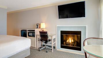 Habitación de hotel con cama, escritorio con silla, televisor de pantalla plana y chimenea.
