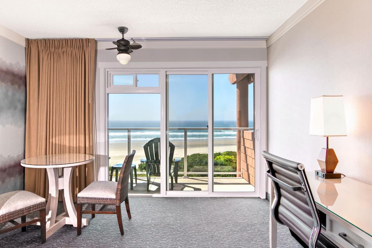 A hotel room with a balcony, a table, two chairs, a lamp, and a view of the ocean.