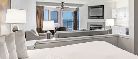 Habitación de hotel con una cama grande, zona de estar con vistas al océano, televisor de pantalla plana y kitchenette.