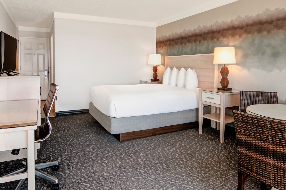 A hotel room with a bed, two bedside tables with lamps, a chair, a desk, and a television.