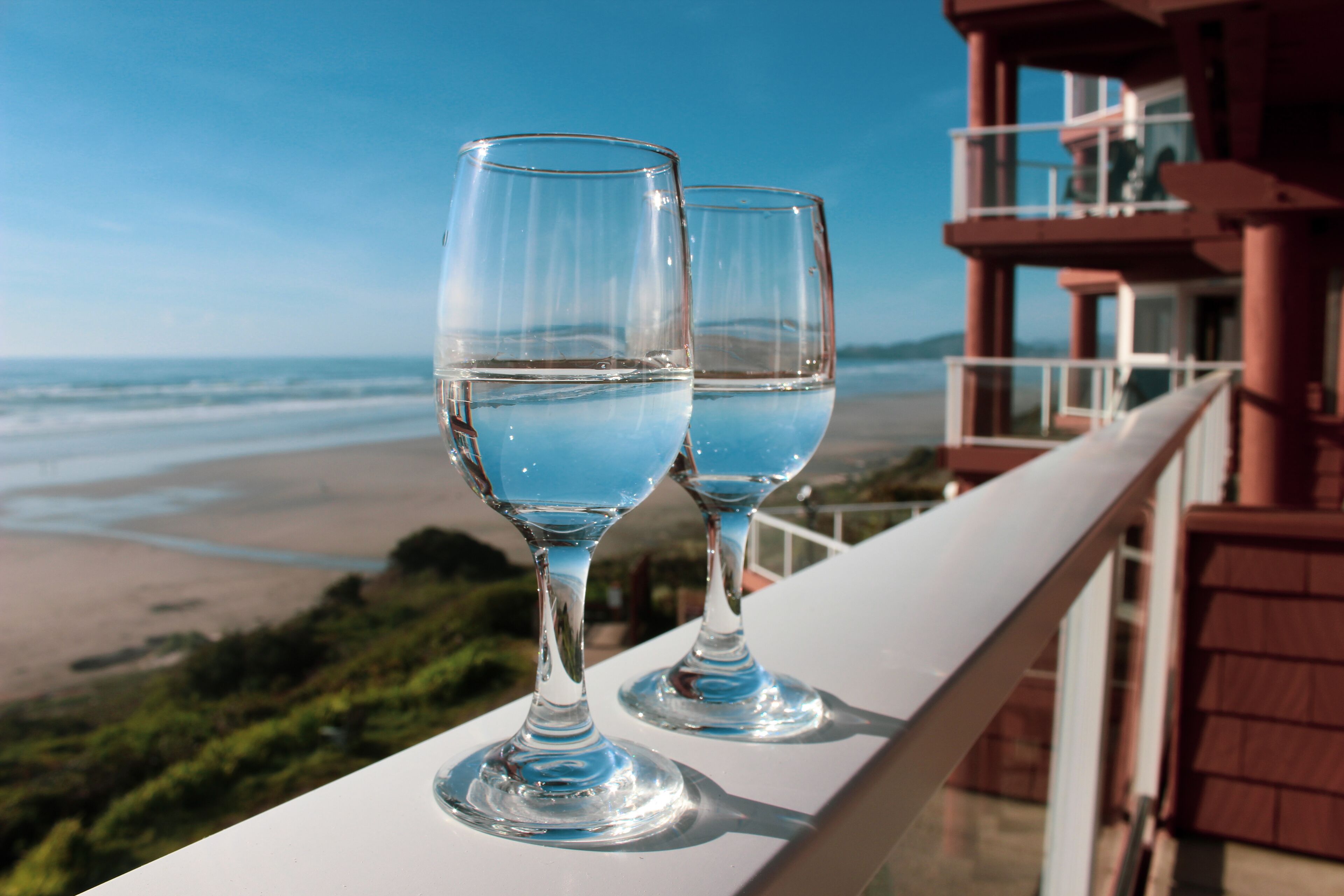 Two glasses of blue liquid on a balcony overlooking a beach.