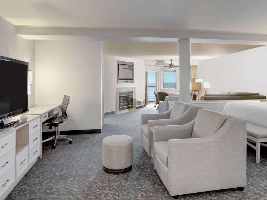 A hotel room with a flat-screen TV, a desk with a chair, a sofa, a bed, and a view of the ocean.