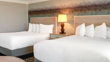 A hotel room with two beds, a nightstand with a lamp, a round table, and a textured wall mural.