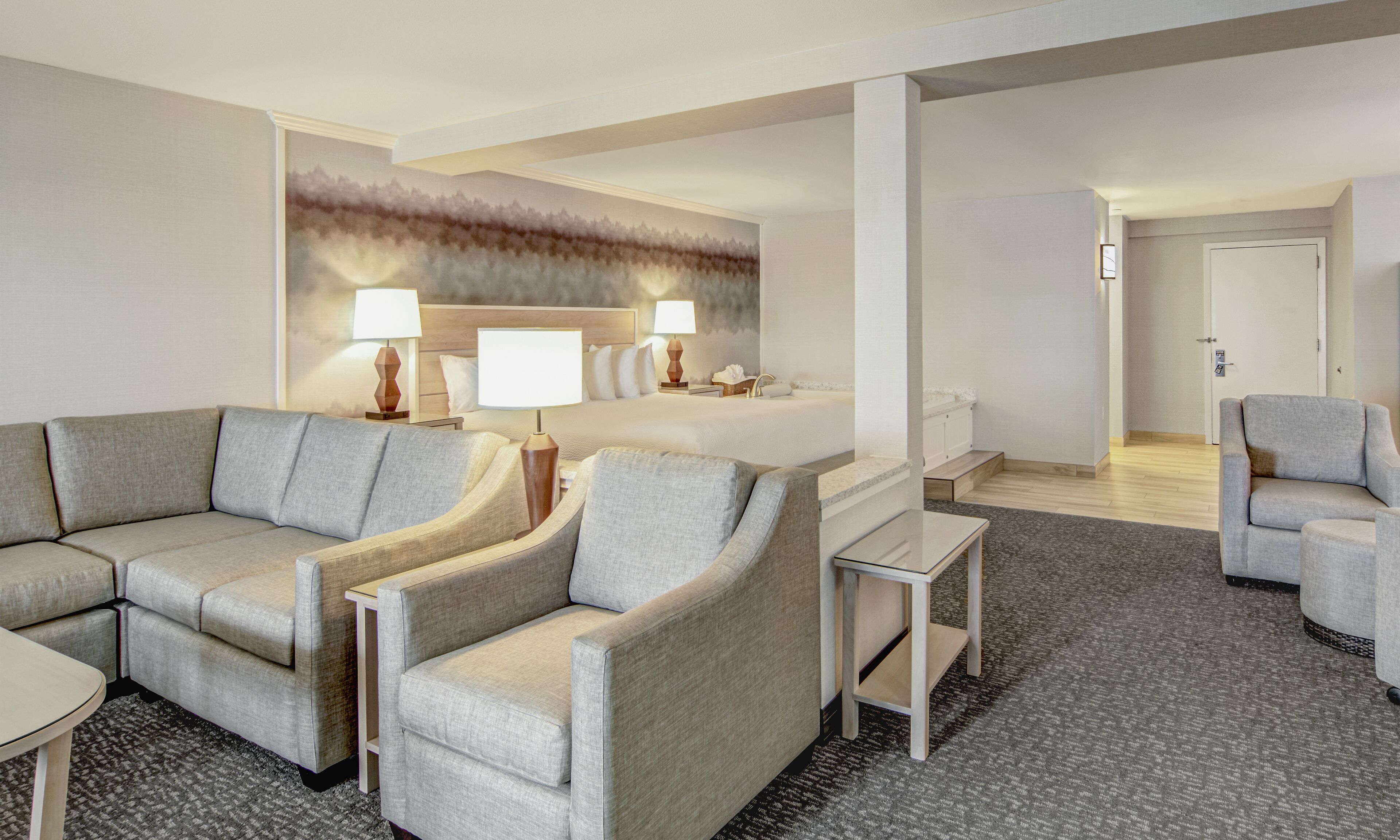 Ein Hotelzimmer mit Sofa, Sesseln, einem kleinen Tisch, einem Bett und einem Badezimmer.