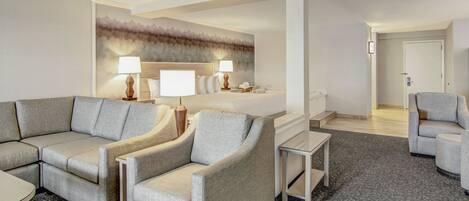 A hotel room with a sofa, armchairs, a small table, a bed, and a bathroom.