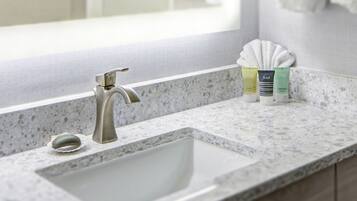 Un baño con un lavamanos blanco, un solo grifo y artículos de aseo en la encimera.