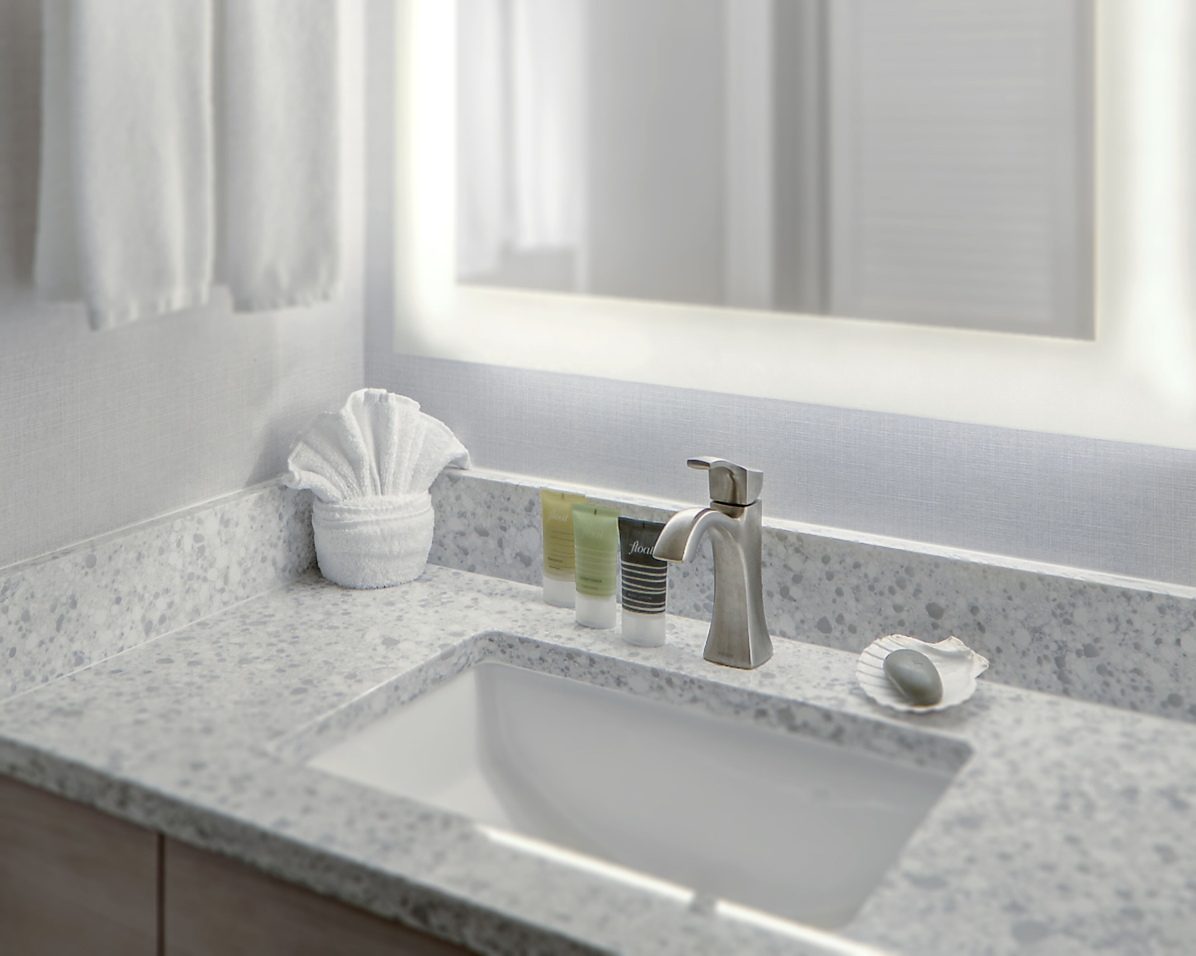 A bathroom with a marble sink, a towel dispenser, and toiletries on the counter.