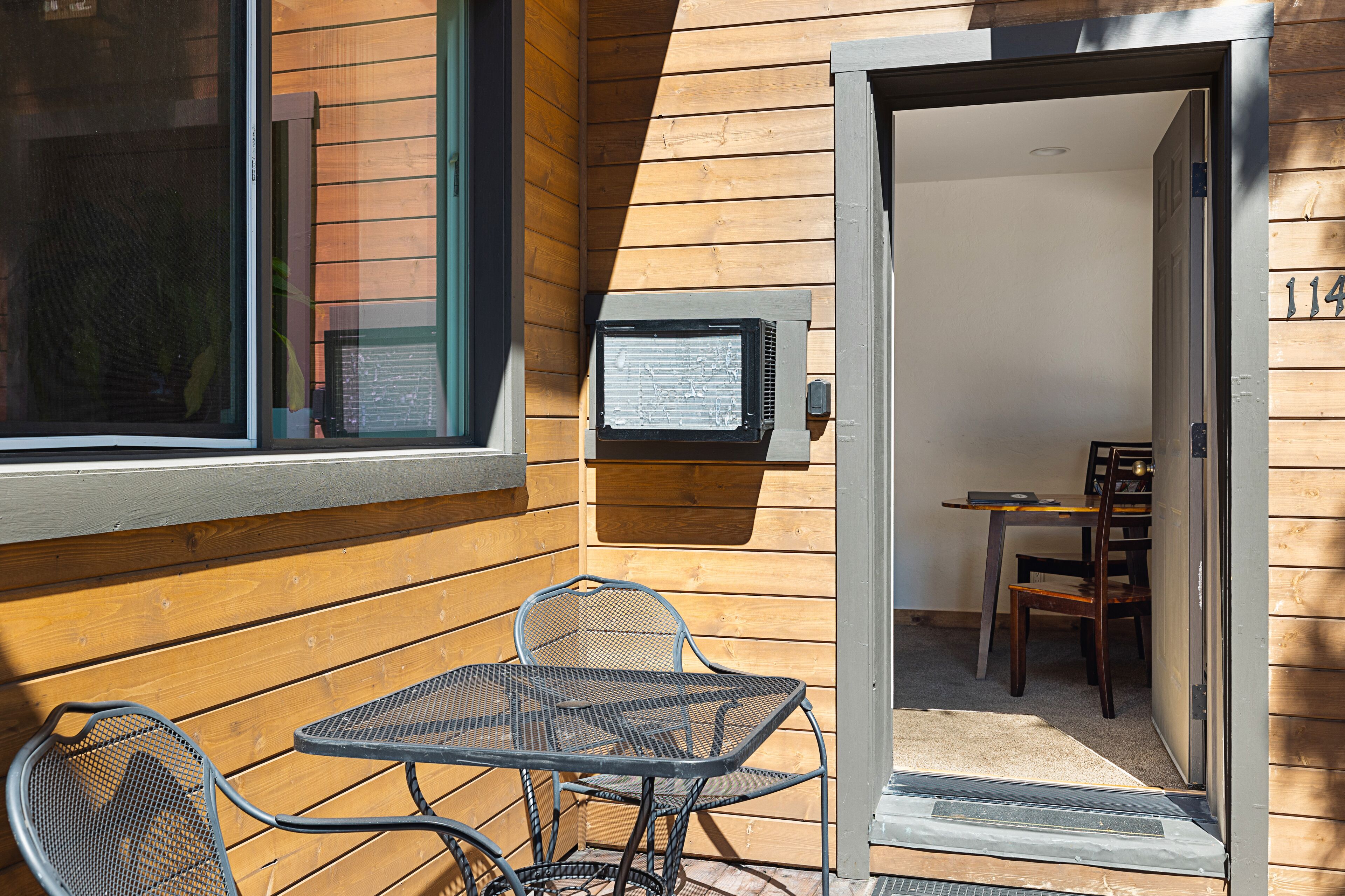 A wooden exterior wall with a window and a door leading to a room with a table and chairs.