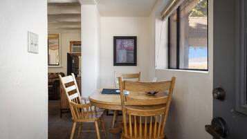 Un coin repas avec une table ronde, des chaises en bois, un tableau encadré au mur et une fenêtre donnant sur un paysage.