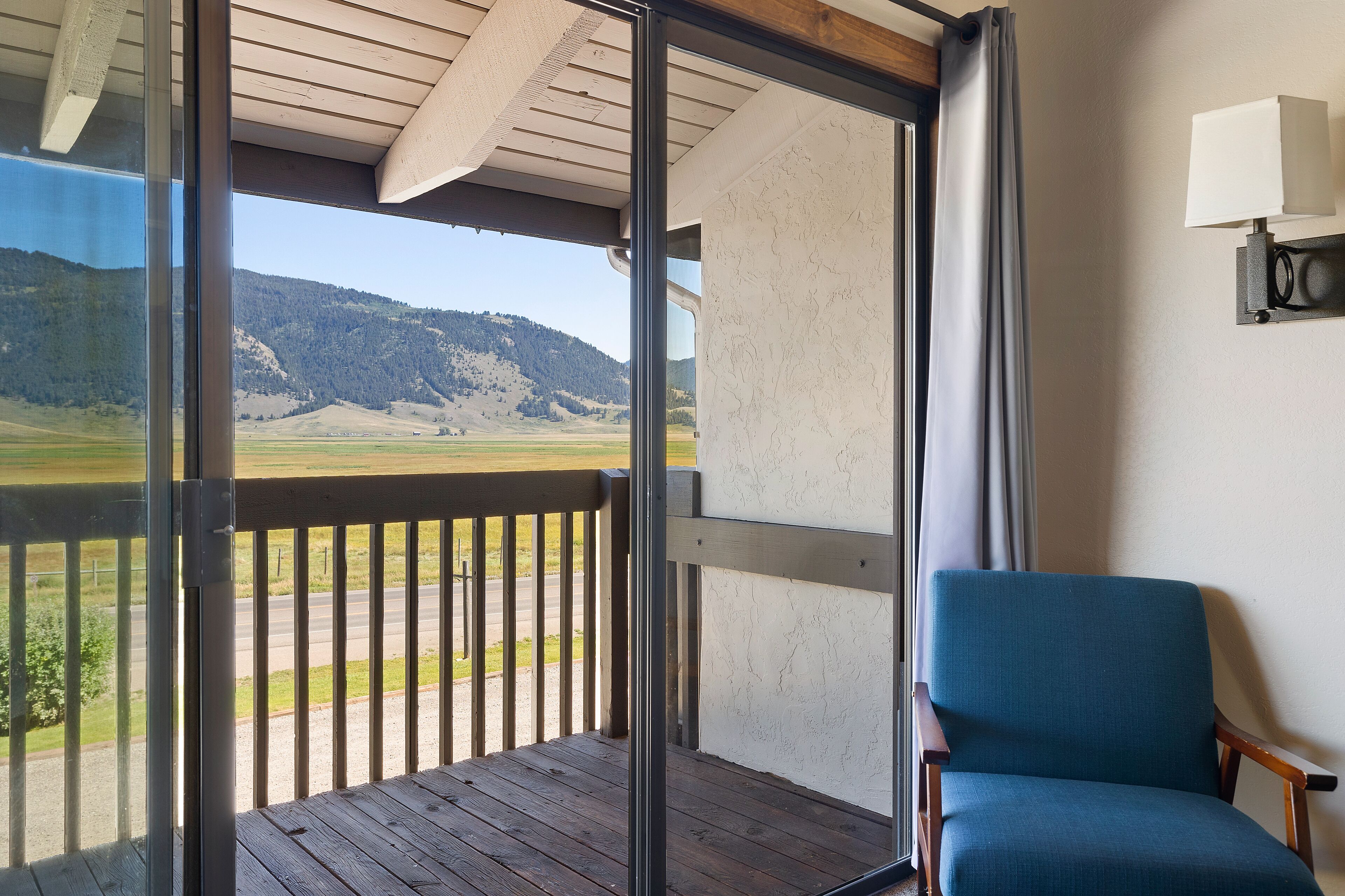 Un balcone con vista su un paesaggio montuoso, una sedia di legno e una lampada fissata al muro.
