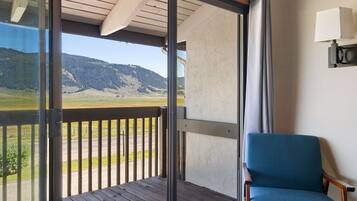 Un balcone con vista su un paesaggio montuoso, una sedia di legno e una lampada fissata al muro.