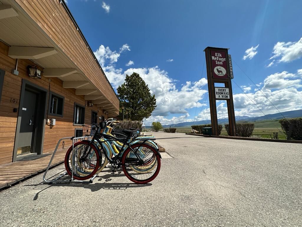 A building with a sign for Elk Refuge Inn, a bike parked in front, and a view of the landscape.