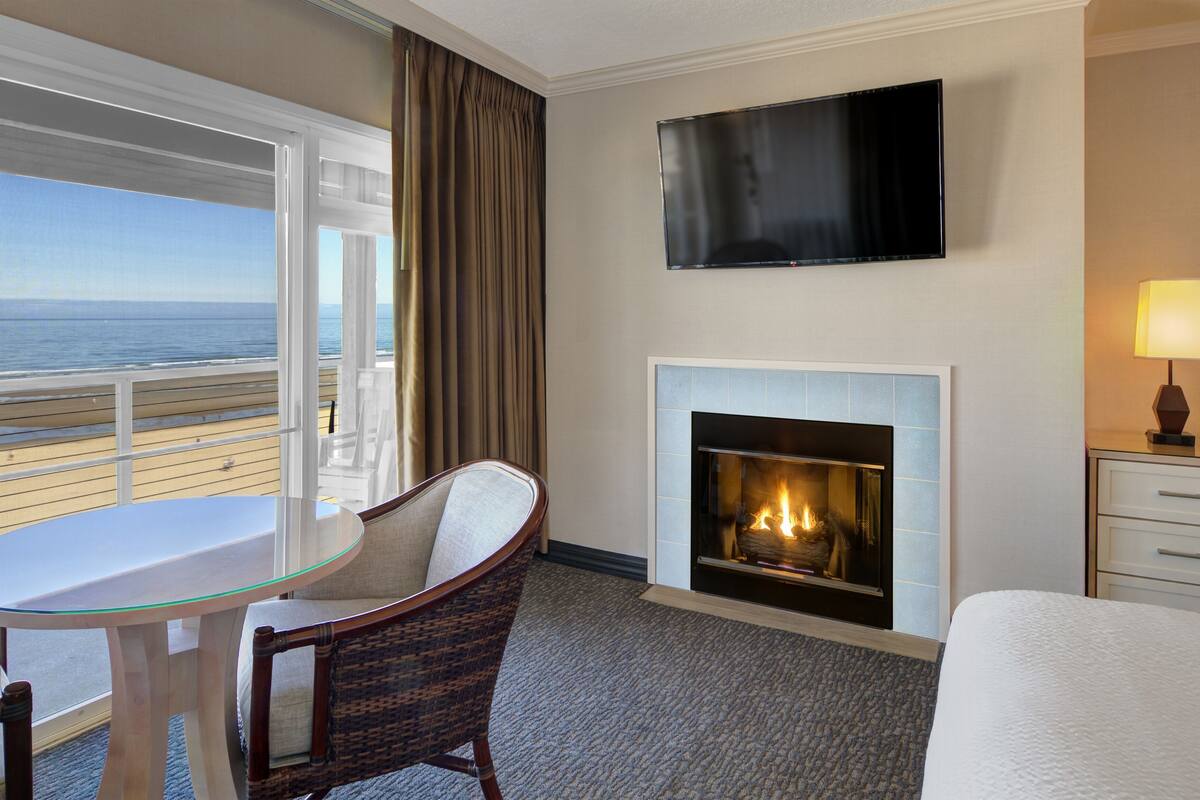 A hotel room with a balcony, a fireplace, a TV, and a table with chairs.