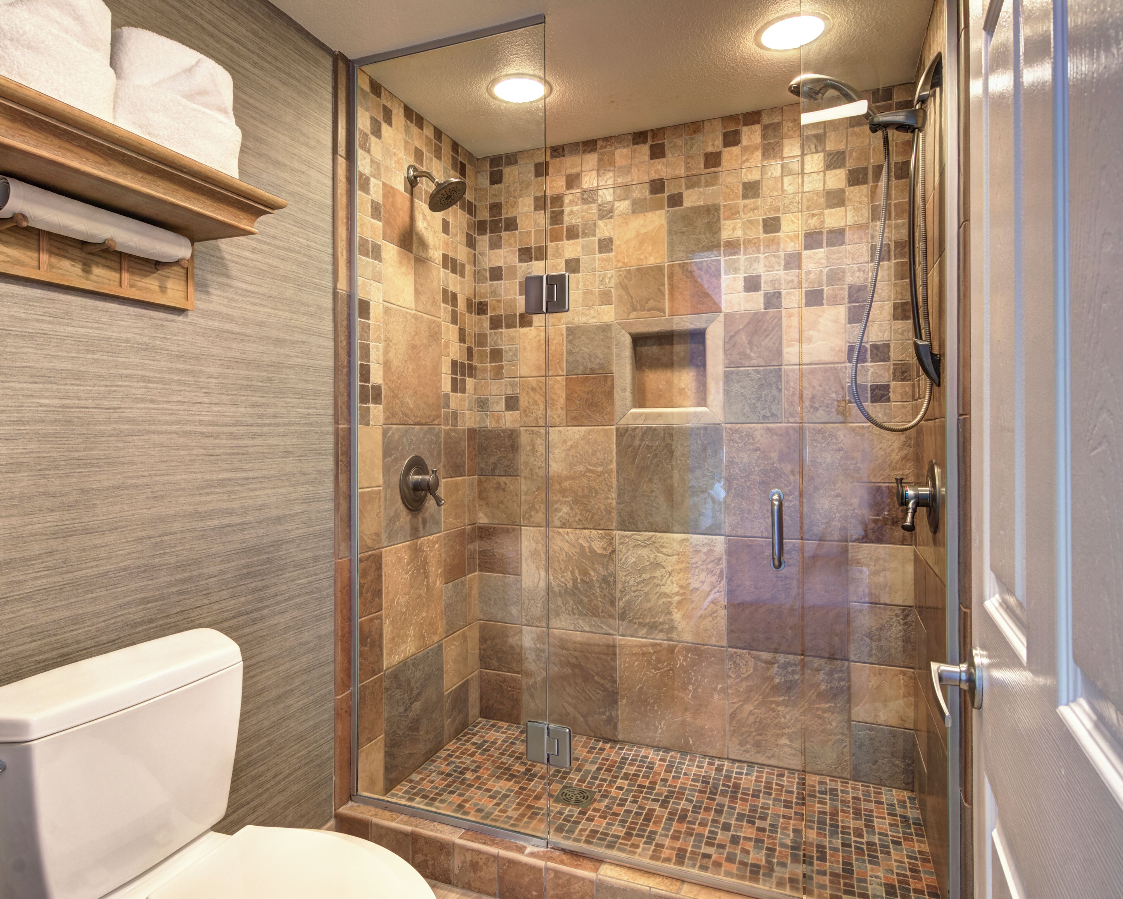 A modern shower with a glass door, a tiled floor, and a wooden shelf with towels.