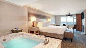 A hotel room with a large bed, a bathtub, a desk, and a view of the ocean.