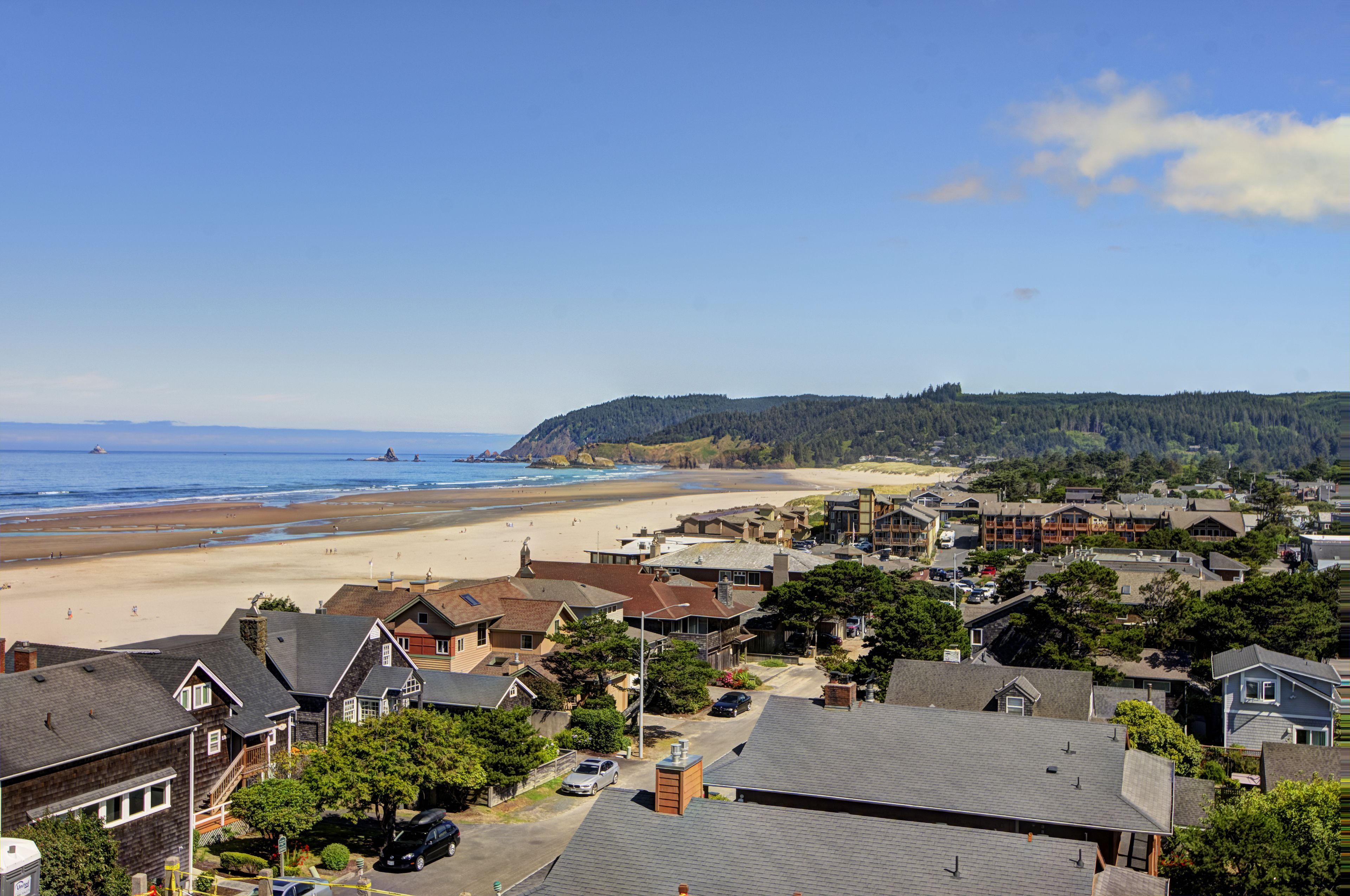 Un pueblo costero con playa, casas y una colina boscosa.