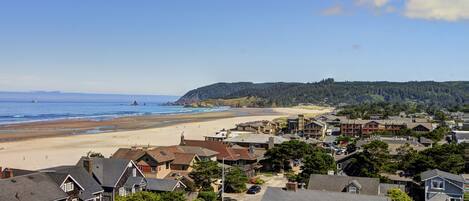 Un pueblo costero con playa, casas y una colina boscosa.