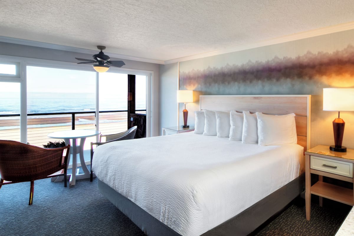 A hotel room with a large bed, two bedside tables, a chair, and a view of the beach.