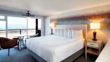 Een hotelkamer met een groot bed, twee nachtkastjes, een stoel en uitzicht op het strand.