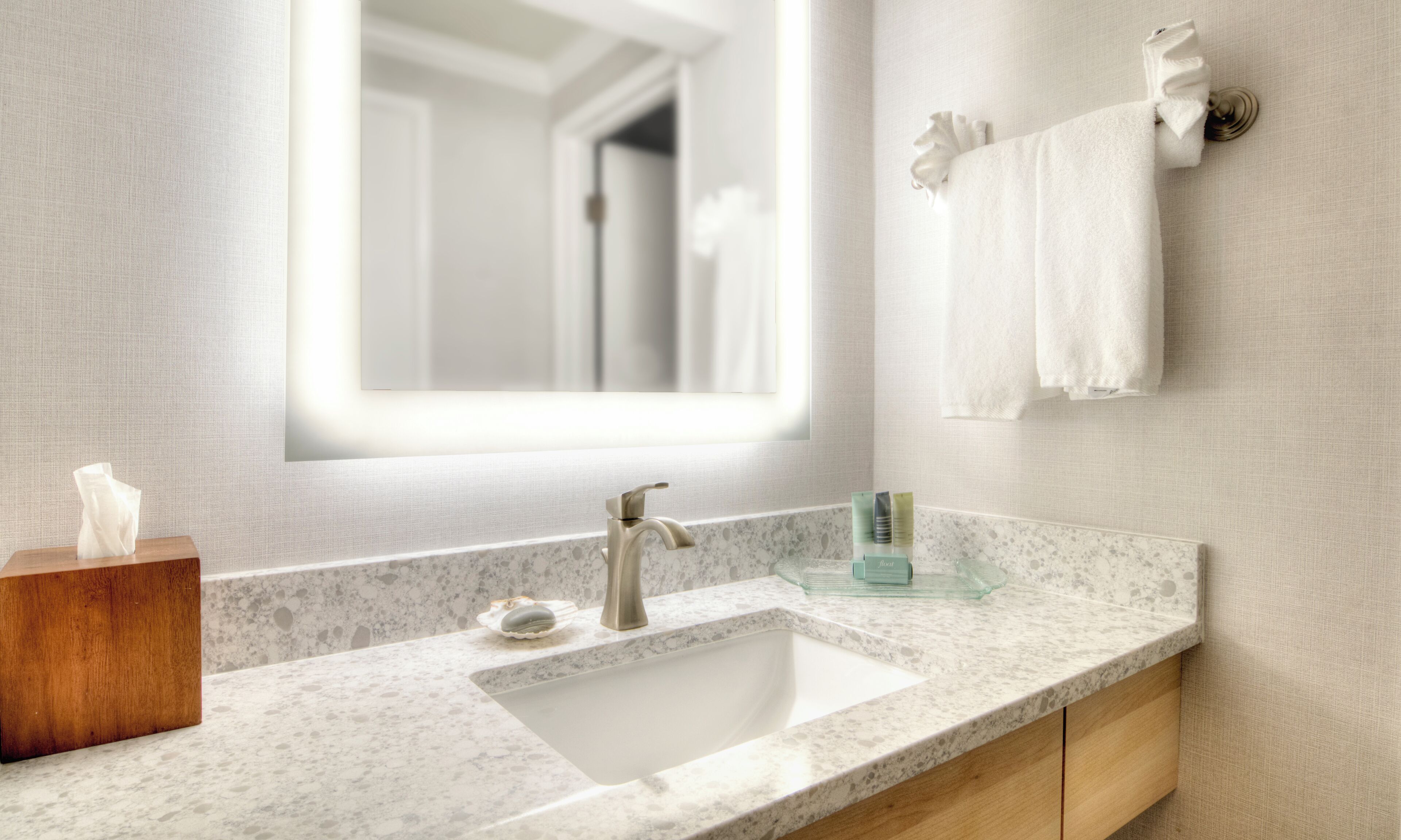A modern bathroom with a marble sink, a large mirror, and a towel rack.