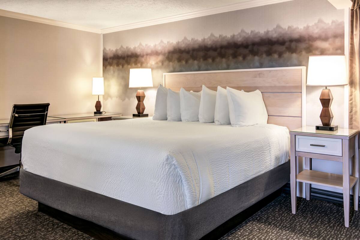 A hotel room with a large bed, two bedside tables with lamps, a chair, and a desk.