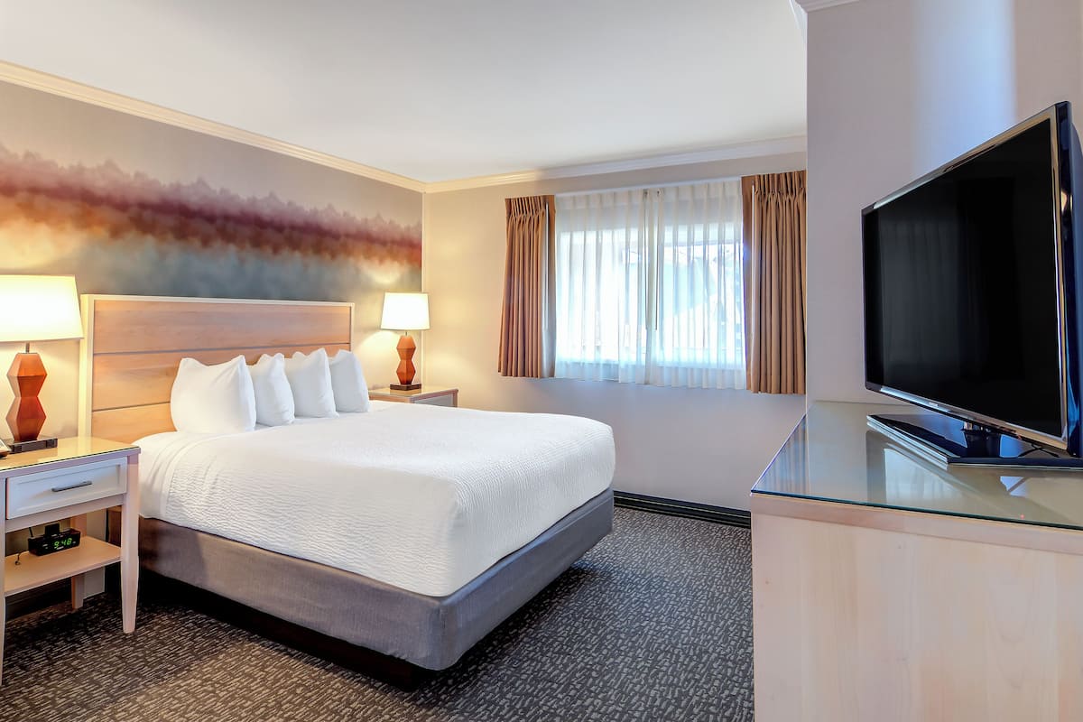 A hotel room with a large bed, a flat-screen TV, a nightstand, a lamp, and a window with curtains.
