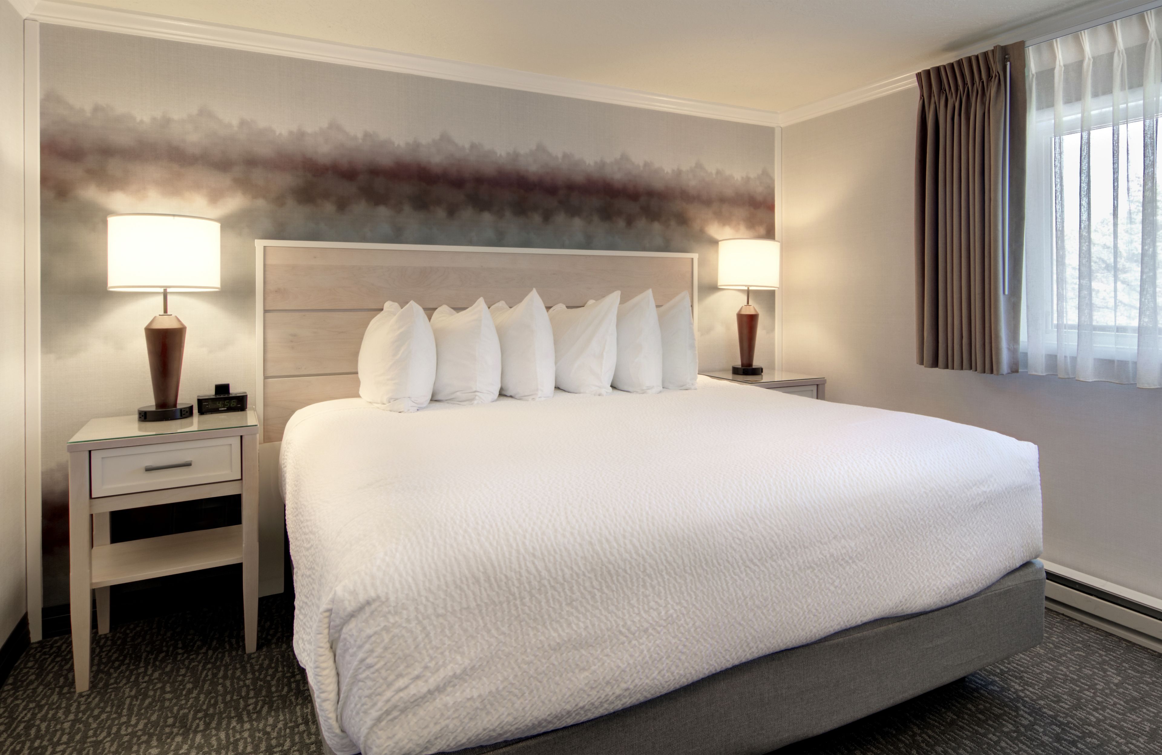 A large bed with a wooden headboard, two bedside tables with lamps, and a wall with a textured mural.