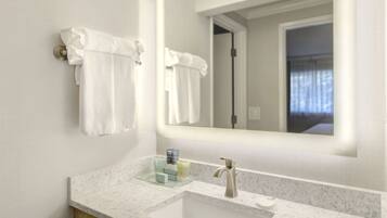 A bathroom with a white sink, a mirror, and two white towels hanging on hooks.