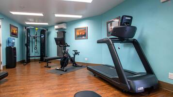 Een sportschool met een loopband, een hometrainer en krachttoestellen.