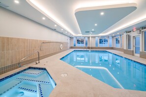 A large indoor swimming pool with a separate hot tub area, tiled walls, and a modern ceiling design.