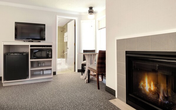A living room with a flat-screen TV, a built-in microwave, a refrigerator, a fireplace, and a dining area with a table and chairs.