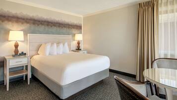 A hotel room with a large bed, two bedside tables with lamps, a chair, and a view of the outdoors through curtains.