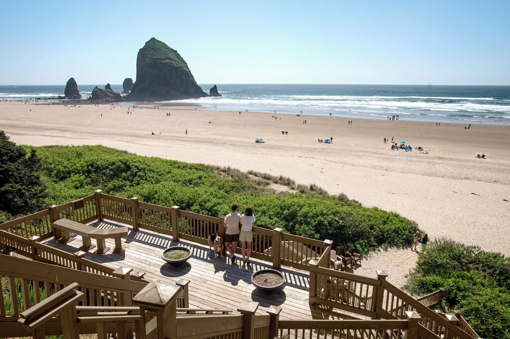 A beach with a wooden deck, benches, and a view of the ocean and rock formations.