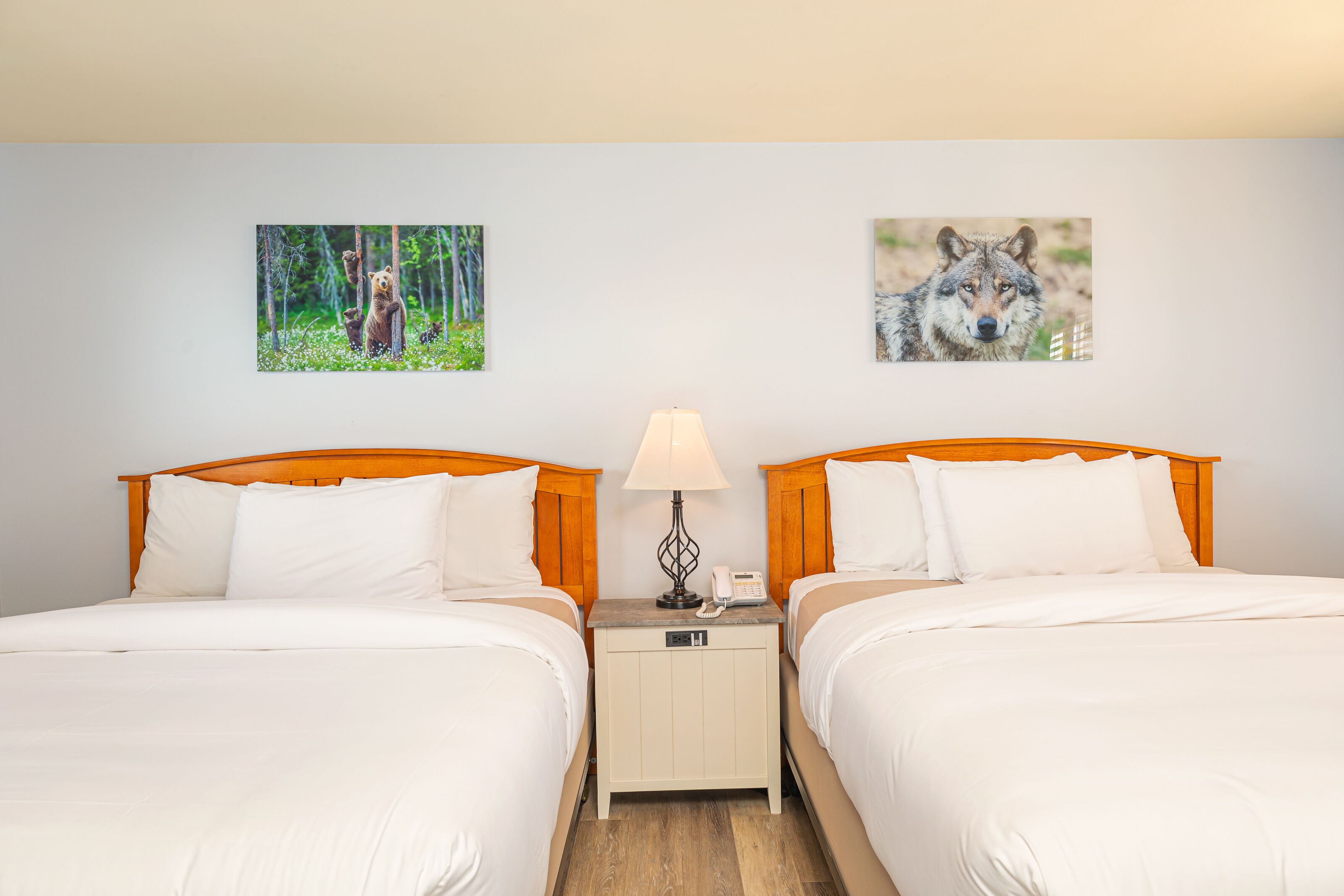 Ein Hotelzimmer mit zwei Betten, einem Nachttisch mit Lampe und zwei gerahmten Bildern an der Wand.