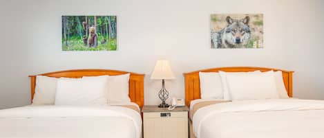 Ein Hotelzimmer mit zwei Betten, einem Nachttisch mit Lampe und zwei gerahmten Bildern an der Wand.
