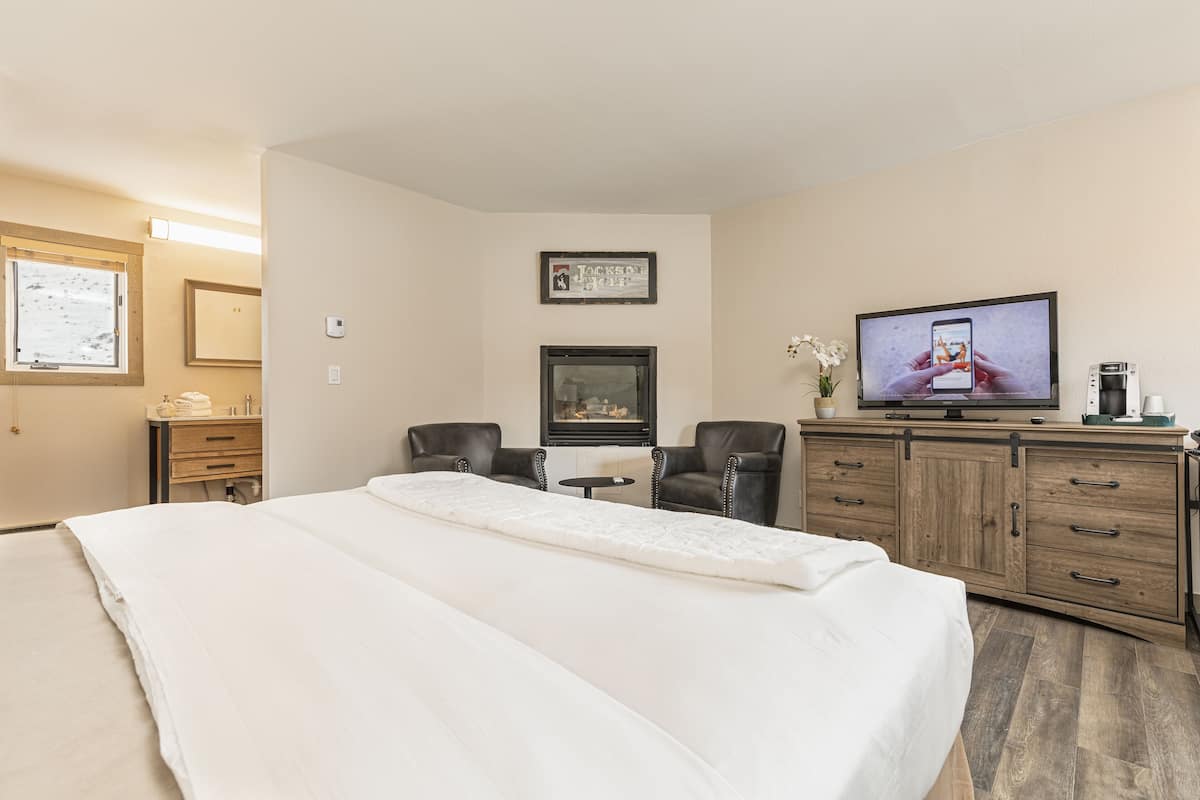 A hotel room with a large bed, a desk with a chair, a television, and a cabinet.