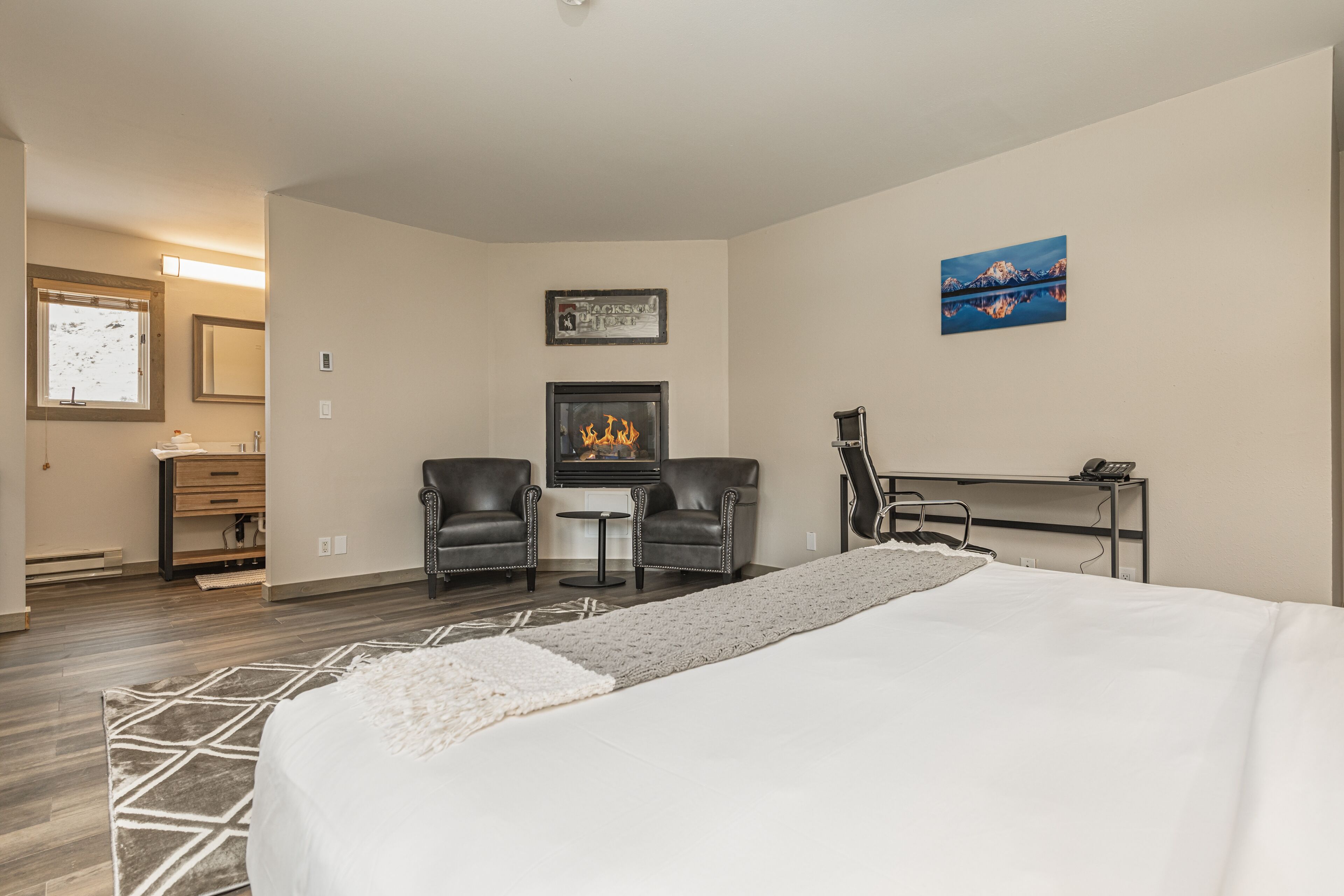 Una habitación de hotel con una cama, dos sillones de cuero, una mesita, una chimenea y un cuadro en la pared.