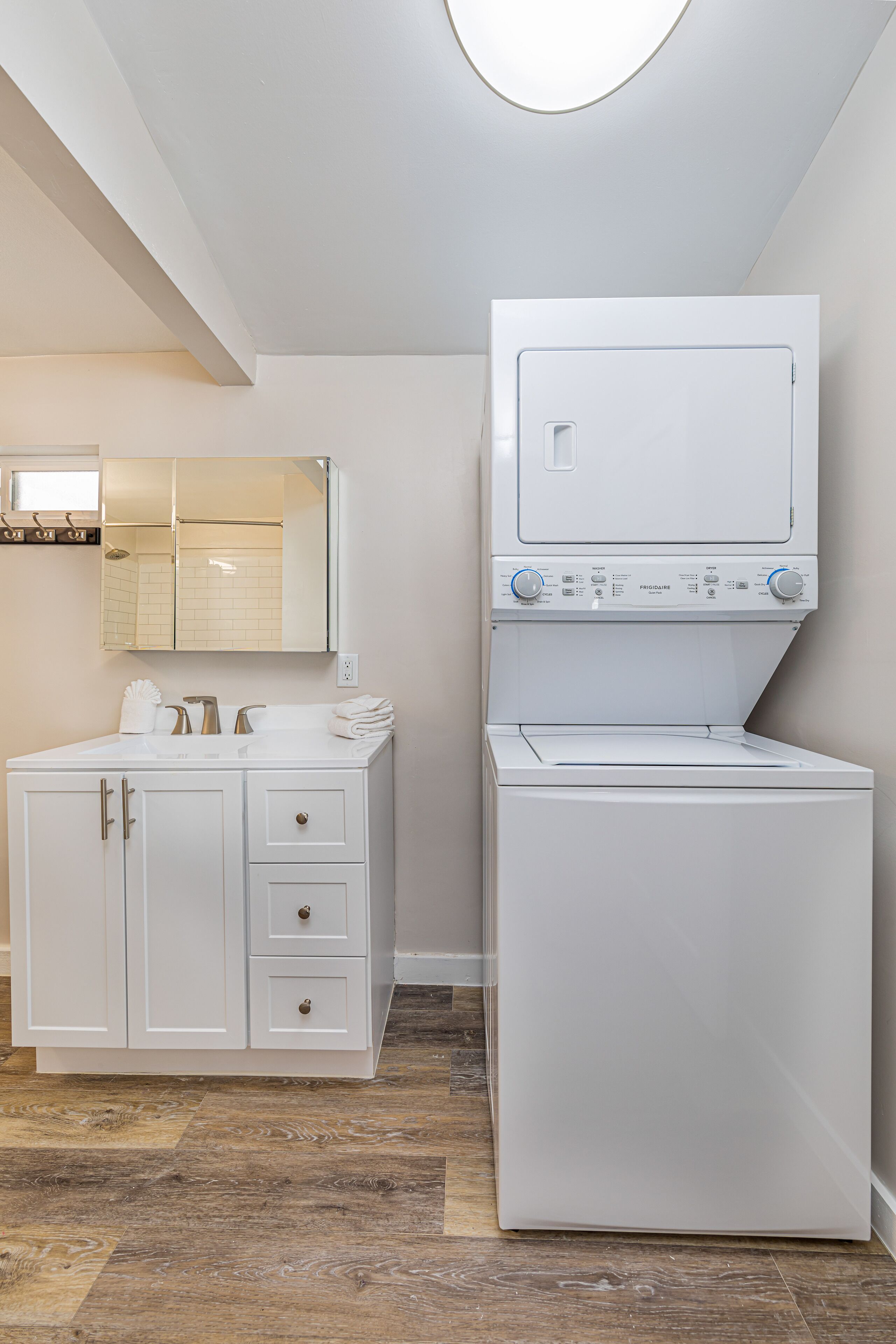 A laundry room with a white washing machine and dryer, a white cabinet with drawers, and a mirror above the sink.