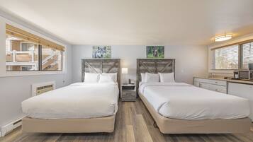 Quarto de hotel com duas camas, mesa de cabeceira, luminária, pequena mesa, micro-ondas e janela com persianas.
