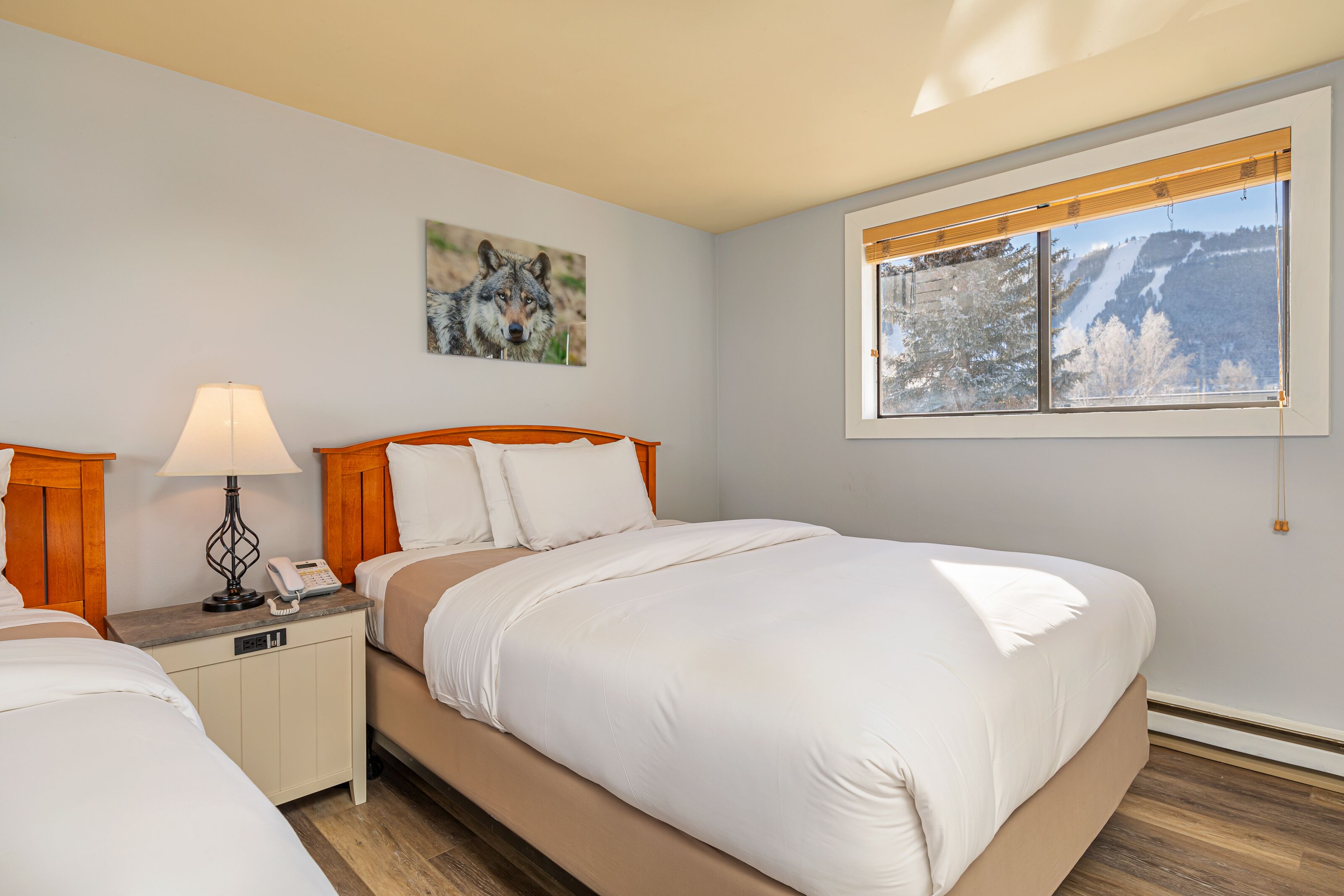 Une chambre à coucher avec un lit, des tables de chevet, une lampe, un tableau et une fenêtre donnant sur la montagne.