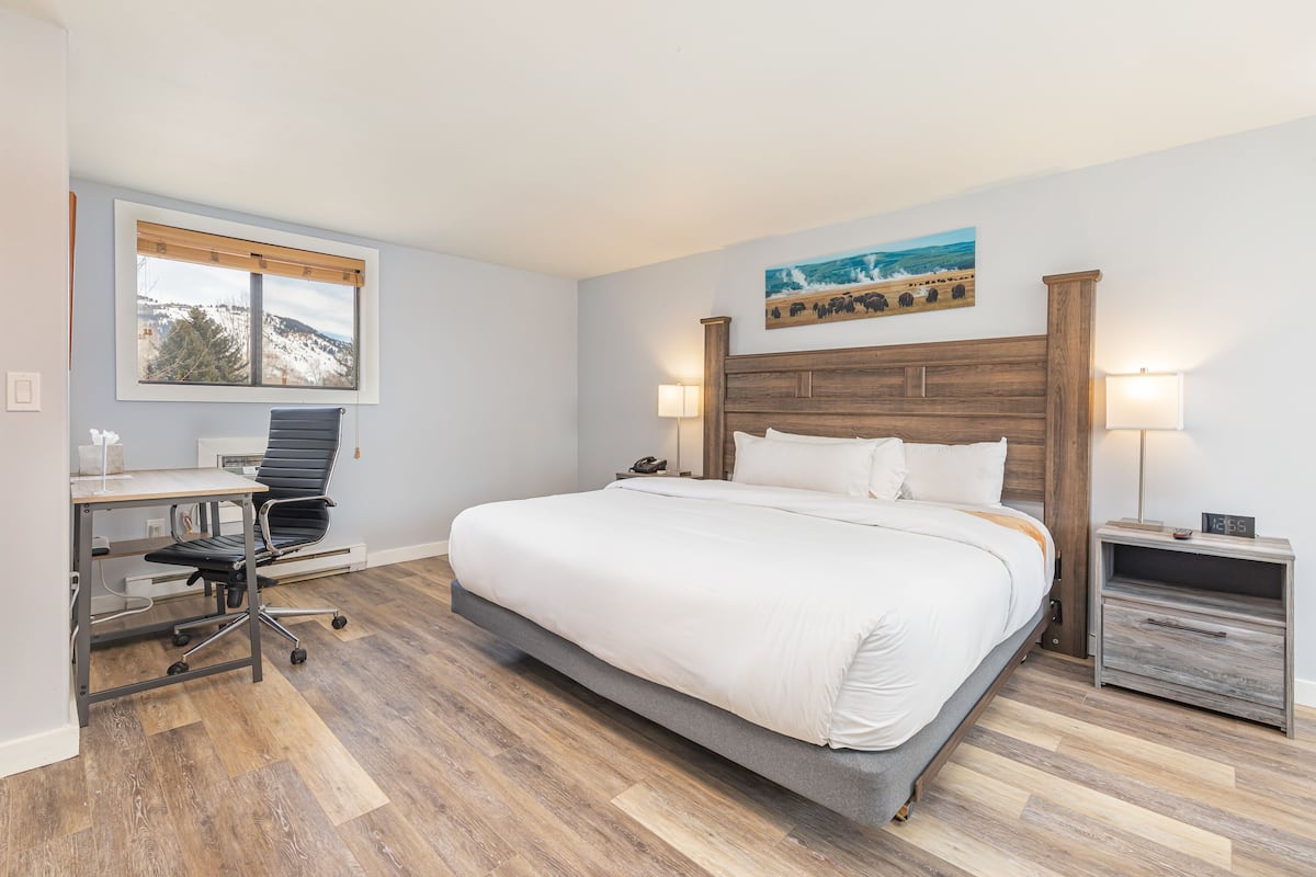 A bedroom with a bed, desk, chair, and a painting on the wall.